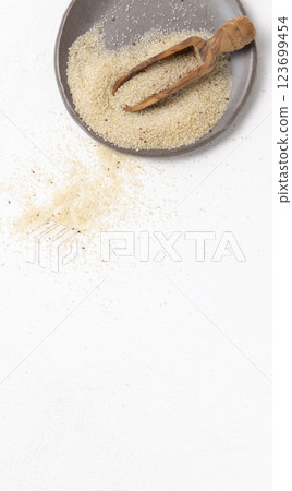 Raw uncooked fonio seeds on grey plate with a wooden scoop on white table topview. African cereal 123699454