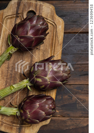 Whole purple raw roman artichokes on a dark wooden table top view. Fresh italian vegetables 123699458