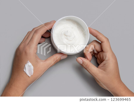 Female hands holding opened cream jar over grey background top view, negative space Female hands holding opened cream jar over grey background top view, negative space 123699465