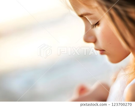 Young girl clutching soft toy, eyes closed, sunset beach softly blurring background, evoking tranquil childhood moment 123700270