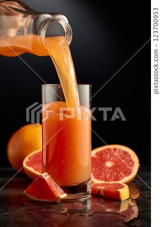 Grapefruit juice is poured from a bottle into a glass. Grapefruit juice is poured from a bottle into a glass. 123700953