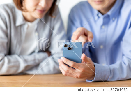 一對中年夫婦在家中一邊看著智慧型手機一邊愉快地交談 一對中年夫婦在家中一邊看著智慧型手機一邊愉快地交談 123701081