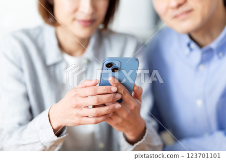 一對中年夫婦在家中一邊看著智慧型手機一邊愉快地交談 123701101