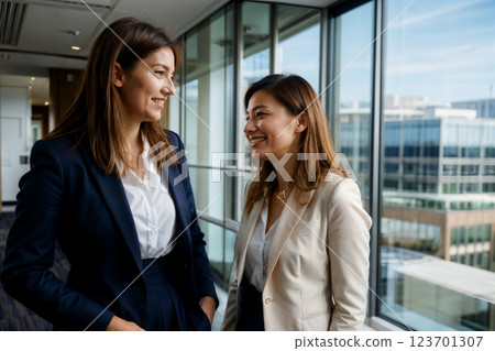 Two professionally dressed women are having a friendly conversation in a modern office setting. Generative ai. Two professionally dressed women are having a friendly conversation in a modern office setting. Generative ai. 123701307