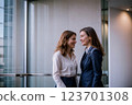 Two professionally dressed women are having a friendly conversation in a modern office setting. Generative ai. 123701308