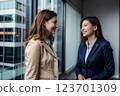 Two professionally dressed women are having a friendly conversation in a modern office setting. Generative ai. 123701309
