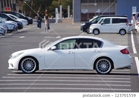 Side view of a D-segment domestic four-door sedan parked in a parking lot at a tourist spot (image with 20-inch wheels) 123701559