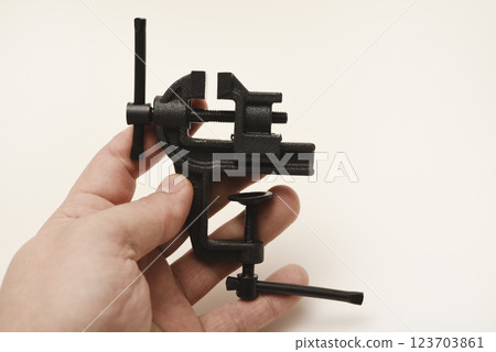A small metal vise in his hand. The clamp. Tooling for locksmithing. A small metal vise in his hand. The clamp. Tooling for locksmithing. 123703861