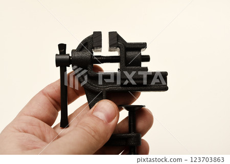 A small metal vise in his hand. The clamp. Tooling for locksmithing. A small metal vise in his hand. The clamp. Tooling for locksmithing. 123703863