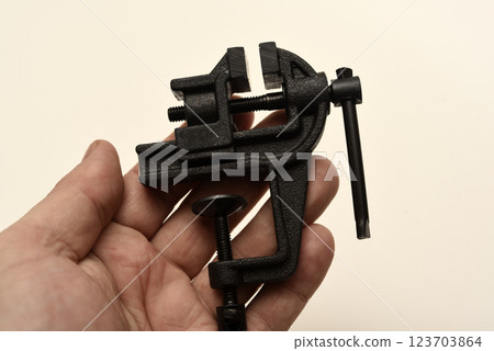 A small metal vise in his hand. The clamp. Tooling for locksmithing. 123703864