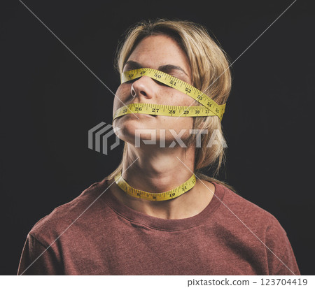 Face, tape measure and stress with an anorexia woman in studio on a dark background for mental health and eating disorder. Sick, hunger and weight with a female struggling with society body pressure Face, tape measure and stress with an anorexia woman in studio on a dark background for mental health and eating disorder. Sick, hunger and weight with a female struggling with society body pressure 123704419