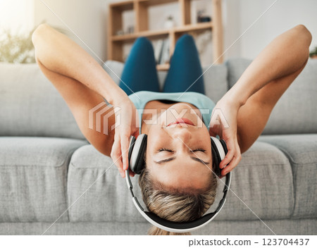 Relax, music and freedom with a woman listening to audio on headphones while lying on a sofa in the living room of her home. Wellness, mental health and streaming with a young female alone in a house 123704437