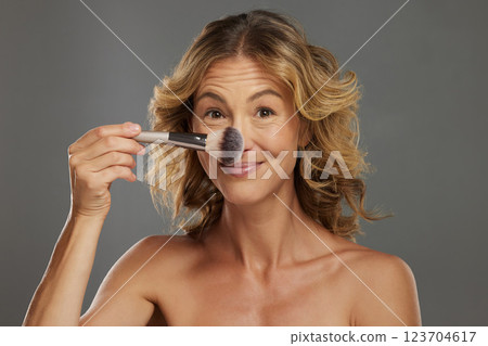 Face, makeup and cosmetics with a woman using a brush in studio on a gray background. Beauty, skin and wellness with an attractive female applying a cosmetic product to her skin for wellness 123704617
