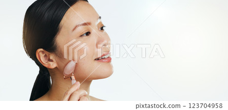 Asian woman, roller and face for skincare beauty, cosmetics or dermatology and anti aging against a white studio background. Happy female model rolling skin for facial treatment, health and wellness Asian woman, roller and face for skincare beauty, cosmetics or dermatology and anti aging against a white studio background. Happy female model rolling skin for facial treatment, health and wellness 123704958