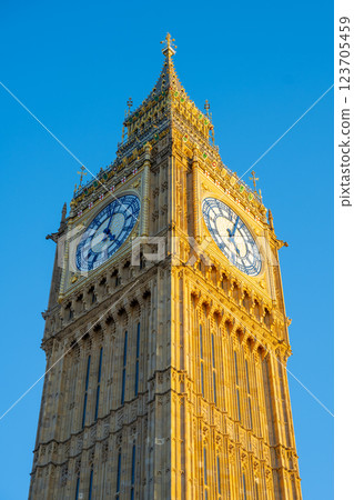Big Ben stands majestically against a clear blue sky in London. The clock tower, with its intricate details, showcases the charm of England and invites admiration from visitors and locals alike. 123705459