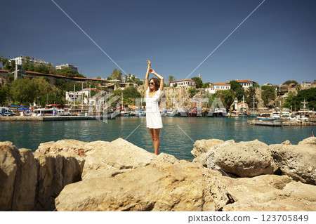 Happy woman in white dress standing on rocks near harbor Happy woman in white dress standing on rocks near harbor 123705849