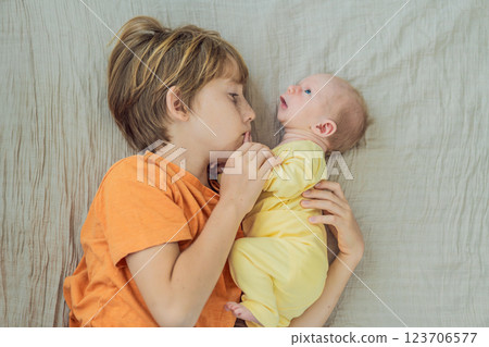 A young boy and his newborn brother lie together on a soft muslin blanket, sharing a tender sibling moment. A heartwarming scene of brotherly love, bonding, and the beginning of a lifelong connection 123706577