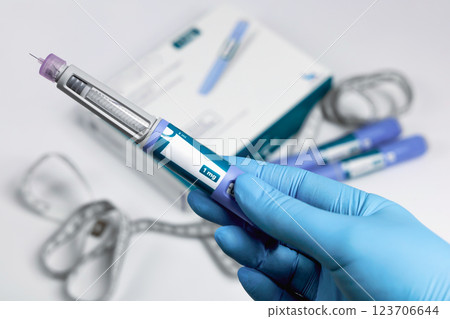 Hands in surgical gloves holding Ozempic Insulin injection pen for diabetics. 123706644