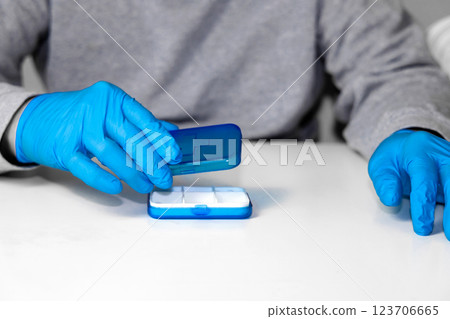 Man in surgical groves with pill organizer. 123706665