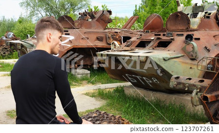 Young man looking at destroyed military equipment of the russian army. Exhibition of rusty and burned-out armored vehicles on ukrainian territory. War between Ukraine and russia. Slow motion Young man looking at destroyed military equipment of the russian army. Exhibition of rusty and burned-out armored vehicles on ukrainian territory. War between Ukraine and russia. Slow motion 123707261