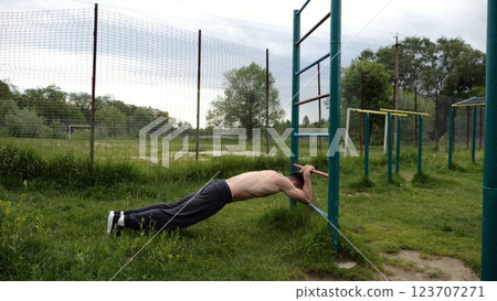 Young muscular athlete doing exercise on triceps at sport equipment outdoor. Male shirtless athlete working out at sport ground. Strong sporty man training at nature. Concept of healthy lifestyle Young muscular athlete doing exercise on triceps at sport equipment outdoor. Male shirtless athlete working out at sport ground. Strong sporty man training at nature. Concept of healthy lifestyle 123707271