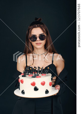 Attractive stylish young girl in black sunglasses holding in hands festive birthday cake Attractive stylish young girl in black sunglasses holding in hands festive birthday cake 123707688