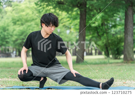 A man in sportswear bends and stretches while warming up before exercising in a park 123710275
