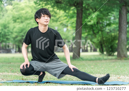 A man in sportswear bends and stretches while warming up before exercising in a park A man in sportswear bends and stretches while warming up before exercising in a park 123710277