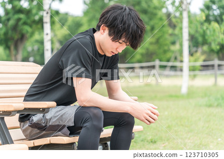 Asian man resting on a park bench during exercise (muscle fatigue, muscle pain, overtraining syndrome) 123710305
