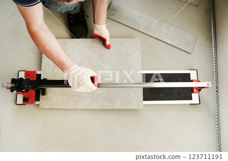 A machine for cutting large ceramic tiles into smaller tiles with precise dimensions. Close-up of the master cutting the tile into two parts with a machine. High quality photo 123711191