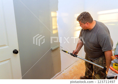 Carpenter is rolling gray paint on wall of bright room, focusing on smooth finish with natural light 123711497