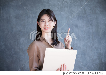 A woman holding a laptop on a dark gray background, smiling and looking at the camera 123711742
