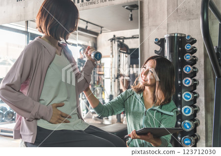 A pregnant woman and her trainer working out, exercising, weight training, dieting and training at a sports gym 123712030