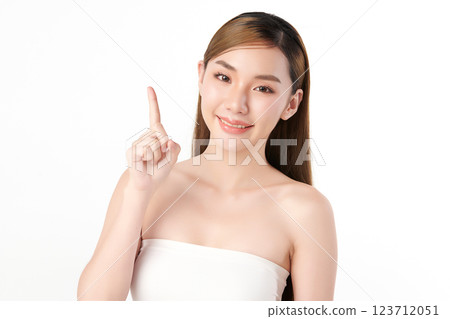 A beautiful Asian woman with clear, radiant skin is raising one finger against a white background. Skincare, beauty, and spa. A beautiful Asian woman with clear, radiant skin is raising one finger against a white background. Skincare, beauty, and spa. 123712051