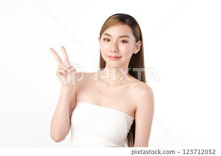Beautiful young Asian woman with clean, fresh skin showing a two-finger gesture on a white background. Face care, beauty, and spa. 123712052