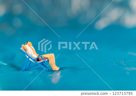 A man lounges on a beach chair, enjoying a peaceful moment on a textured blue surface resembling water 123713795