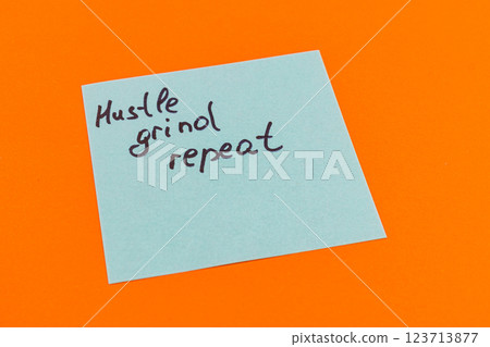 Hustle grind repeat written on a sticky note on vibrant orange background Hustle grind repeat written on a sticky note on vibrant orange background 123713877