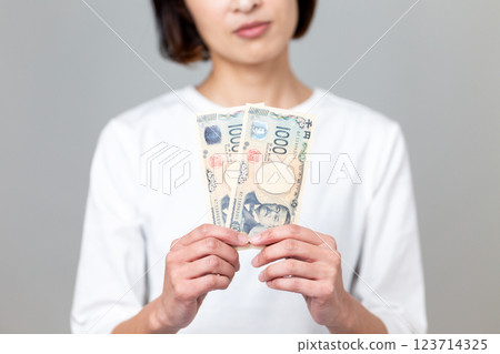 一名中年婦女拿著一張千元鈔票，憂心忡忡 123714325