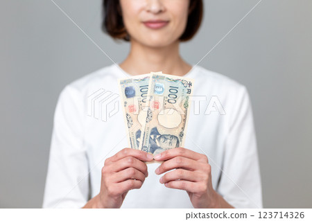 一名中年婦女手持 1000 日元鈔票，面帶微笑 123714326