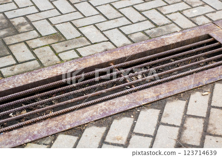 A rusty metal grate is currently sitting on a weathered brick sidewalk 123714639