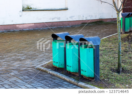 Three green trash cans are neatly lined up in front of a building Three green trash cans are neatly lined up in front of a building 123714645