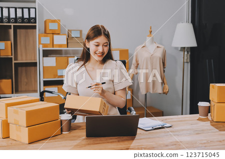 Startup SME small business entrepreneur of freelance Asian woman using a laptop with box Cheerful success Asian woman her hand lifts up online marketing packaging box and delivery SME idea concept 123715045