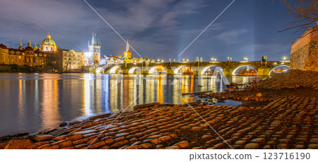 Under the night sky, illuminated Charles Bridge reflects on the calm waters of the Vltava River. Historic buildings line the shore, creating a picturesque atmosphere in Prague. Under the night sky, illuminated Charles Bridge reflects on the calm waters of the Vltava River. Historic buildings line the shore, creating a picturesque atmosphere in Prague. 123716190