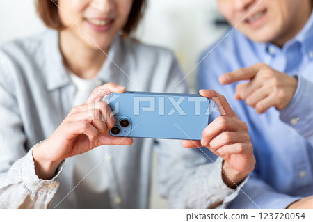 A middle-aged couple happily looking at a smartphone at home A middle-aged couple happily looking at a smartphone at home 123720054