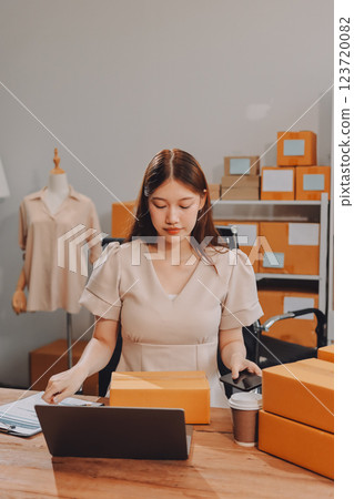 Startup SME small business entrepreneur of freelance Asian woman using a laptop with box Cheerful success Asian woman her hand lifts up online marketing packaging box and delivery SME idea concept 123720082