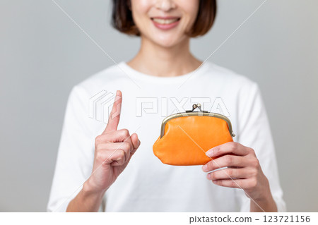 A middle-aged woman holding an orange purse and pointing her index finger up with a smile 123721156