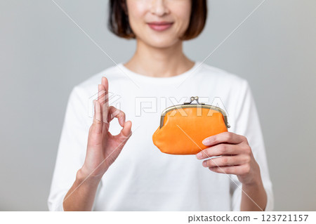 A middle-aged woman smiling and making a circle sign while holding an orange purse 123721157