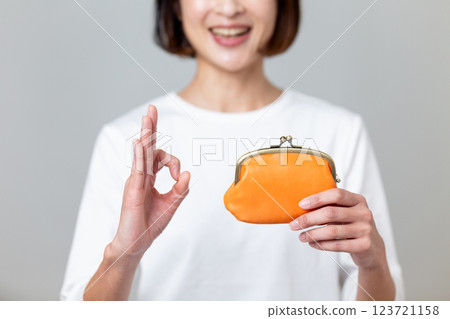 一名中年婦女手持橘色錢包，面帶微笑，比劃著圓圈手勢 123721158