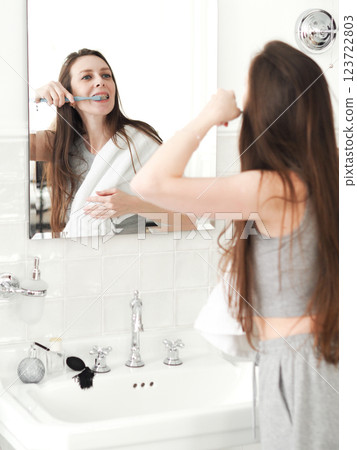 beautiful and young woman with braces, standing in front of the mirror in the bathroom and brushing her teeth 123722803
