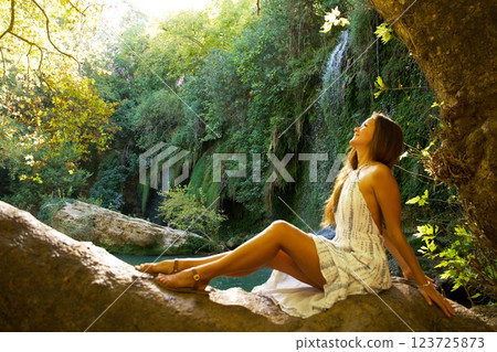 Relaxed Woman Enjoying Nature on Tree Trunk Near Waterfall Relaxed Woman Enjoying Nature on Tree Trunk Near Waterfall 123725873